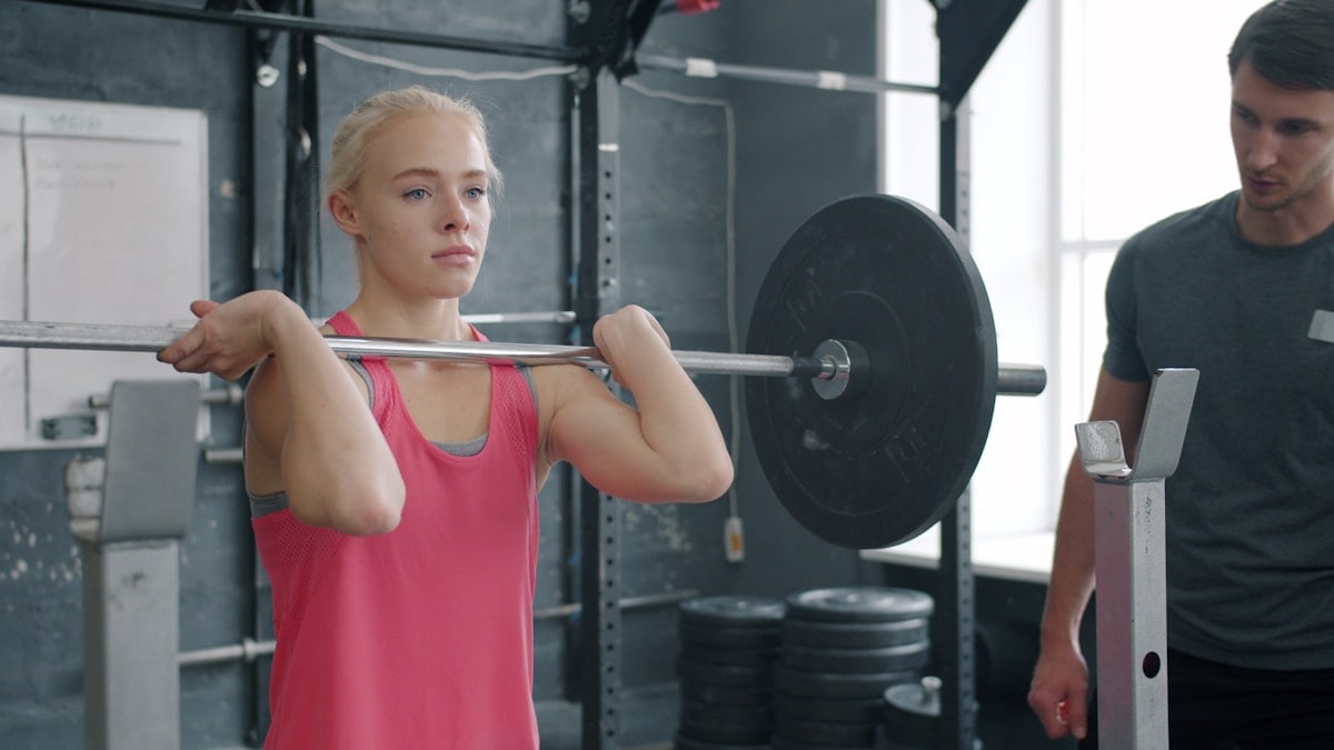 strong young woman doing barbell squats training with instructor in gym. Sports people, active lifestyle and bodybuilding concept.